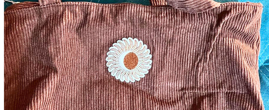 Bolsa marrom em veludo cotelê com alça dupla e aplicação frontal.