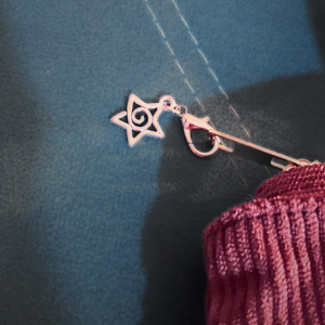 Pingente circular metálico pendurado na alça da bolsa.